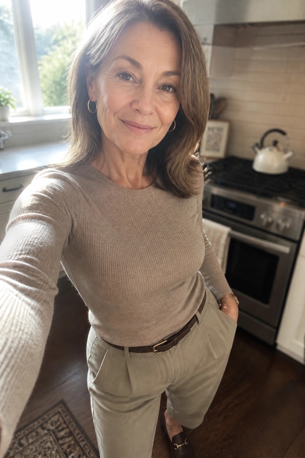 Woman in beige sweater and light pants taking selfie in kitchen