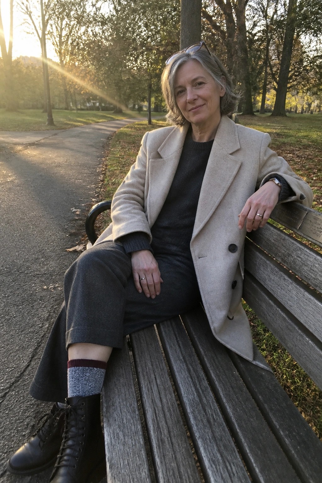 Woman with gray hair in beige coat seated on wooden park bench in sunlight