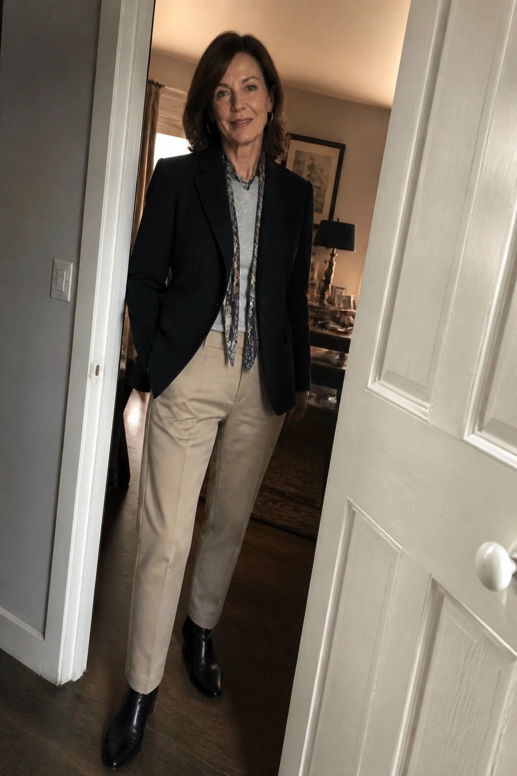 Woman in black blazer, patterned scarf, and beige pants standing in doorway