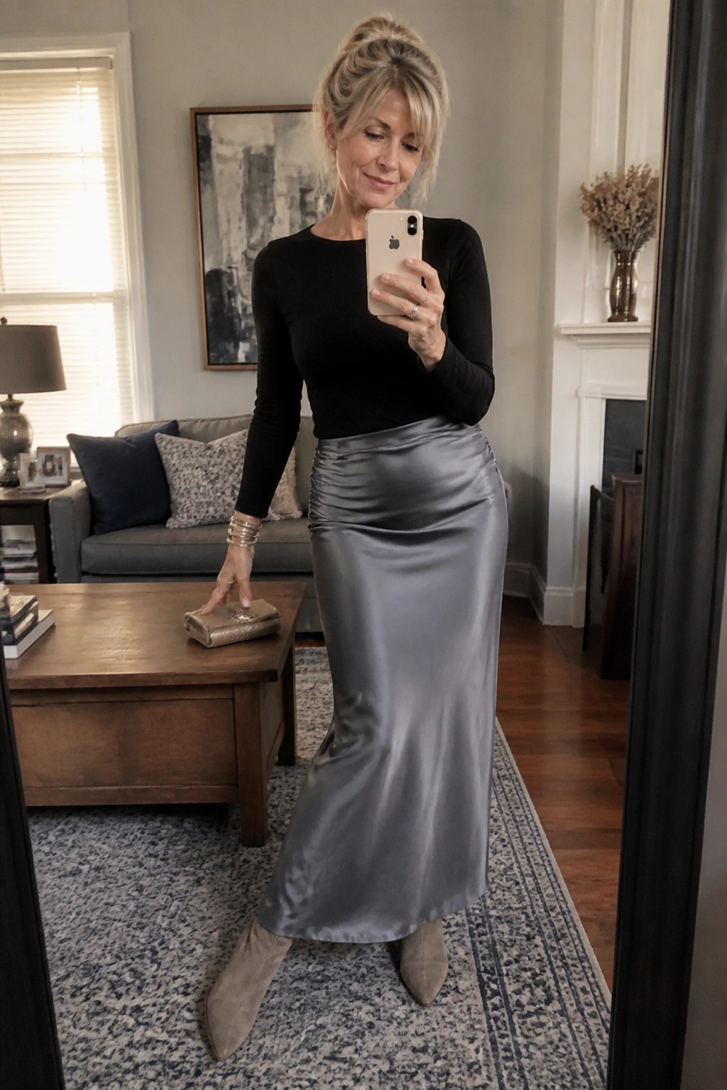 Woman in black top and gray satin skirt taking mirror selfie in living room