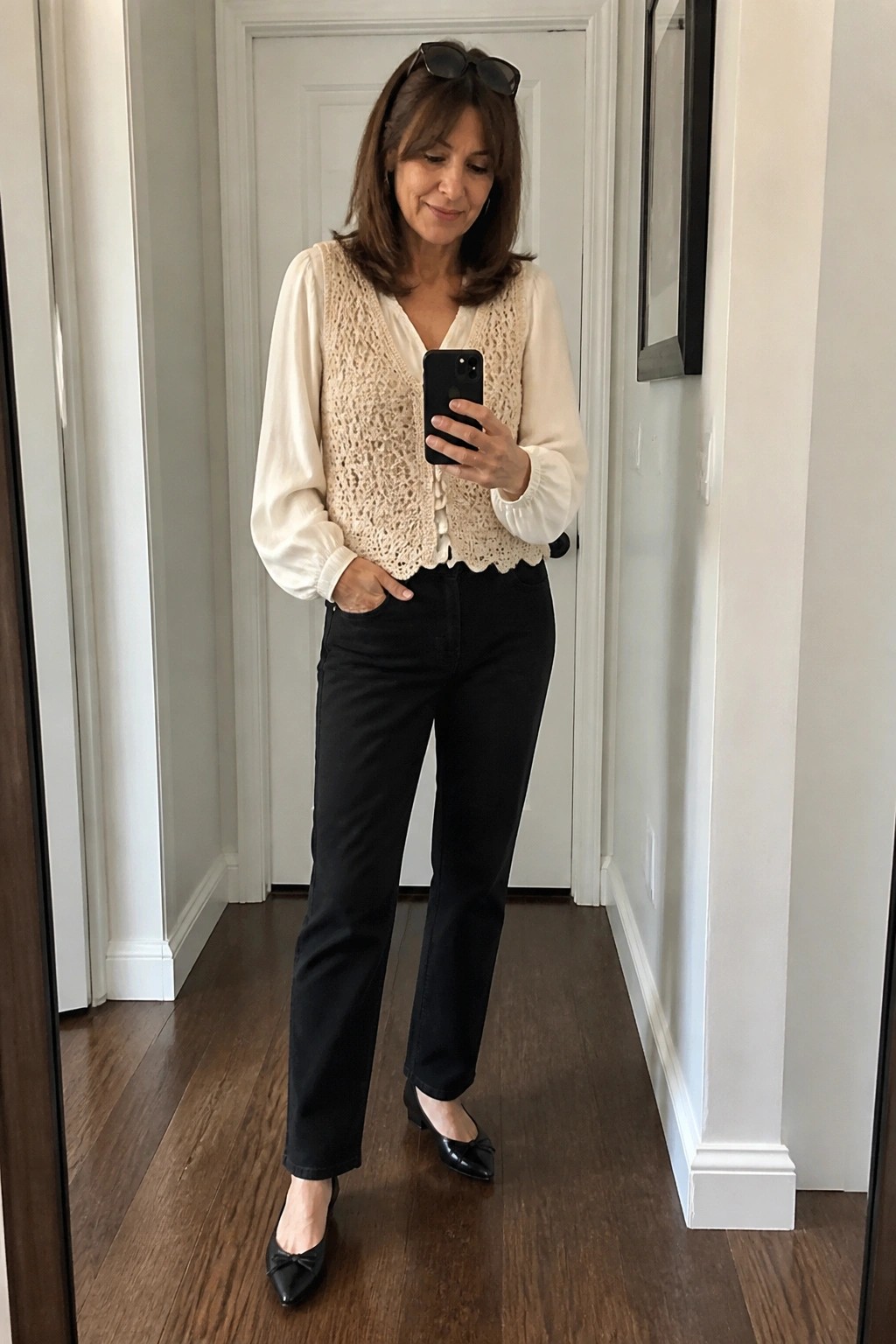 Woman in cream lace vest over white blouse with black jeans taking mirror selfie