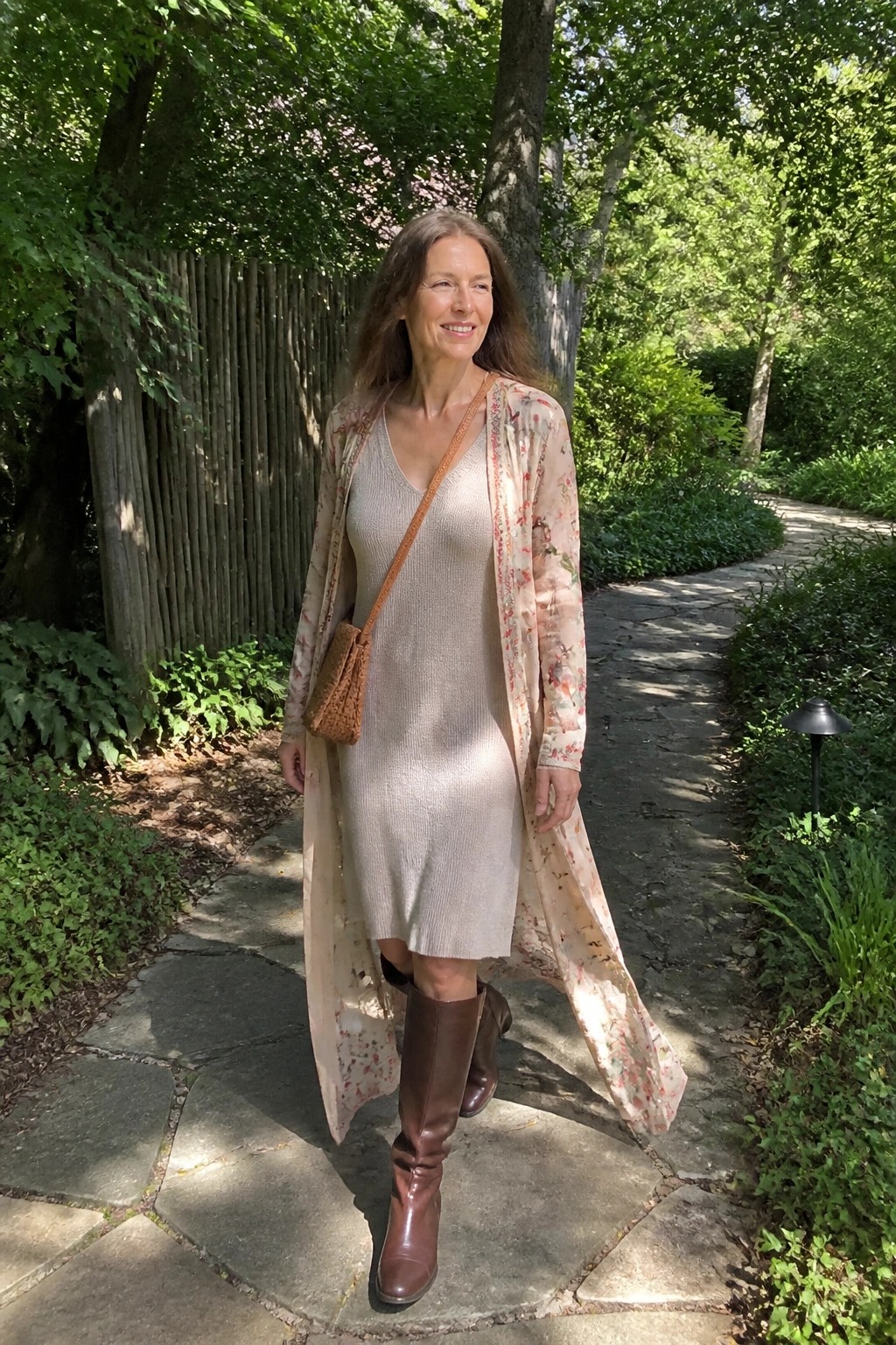 Woman in beige knit dress, floral duster, and brown boots on garden path