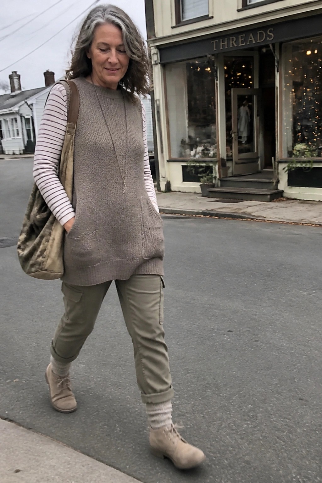 Gray-haired woman in beige knit vest over striped shirt with cargo pants and bag