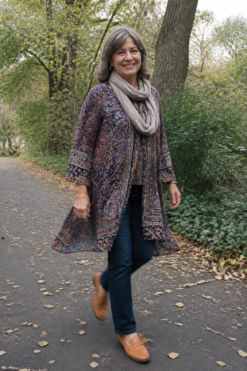 Smiling gray-haired woman in colorful patterned coat walks on autumn path