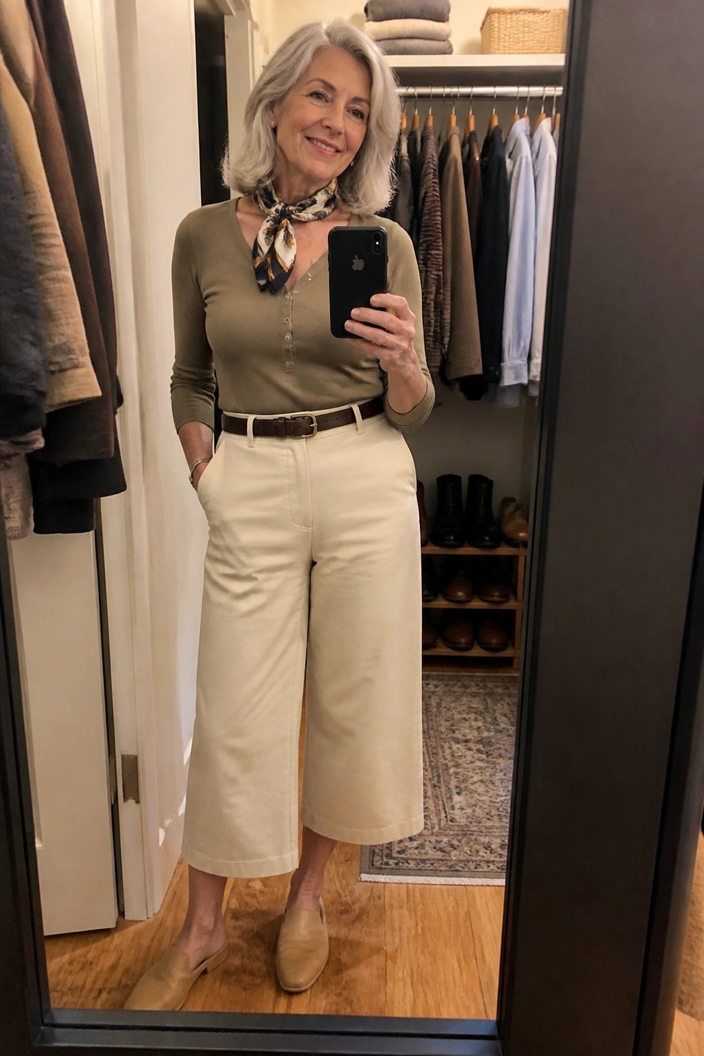 Woman with gray hair in green top and cream pants taking closet mirror selfie
