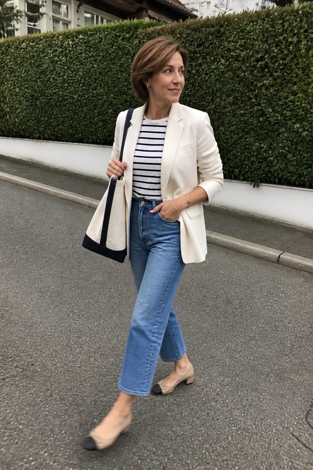 Woman in white blazer and striped shirt carrying tote bag on street