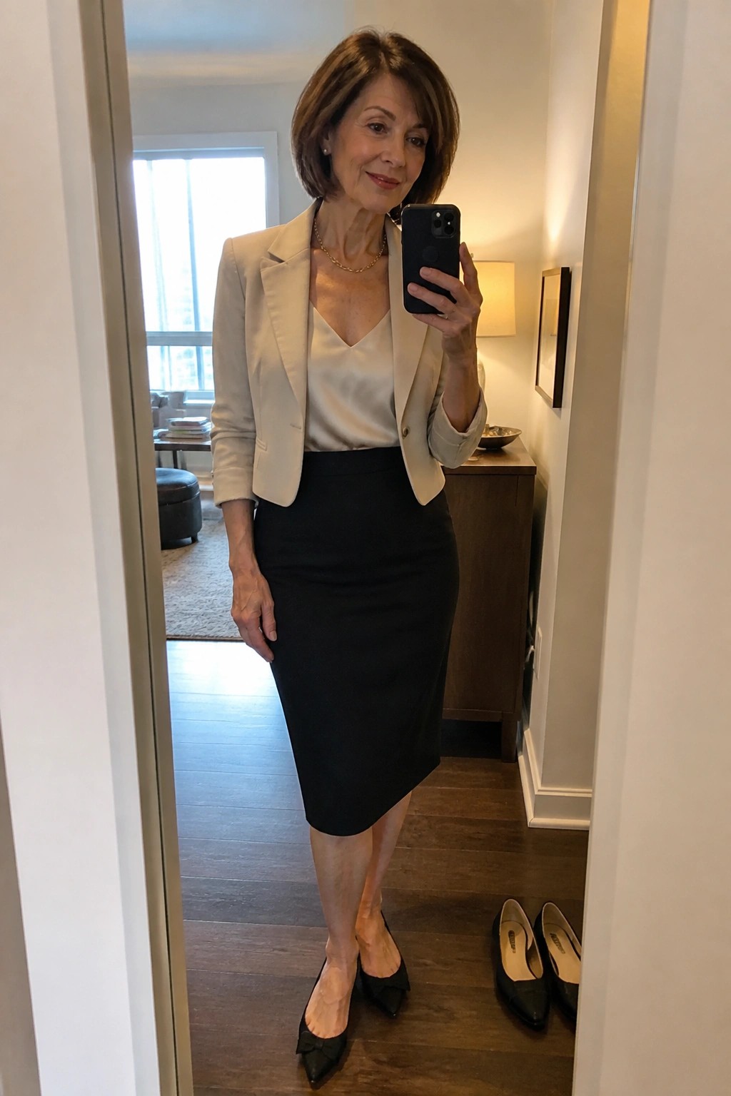 Woman in beige blazer and black skirt taking mirror selfie with smartphone