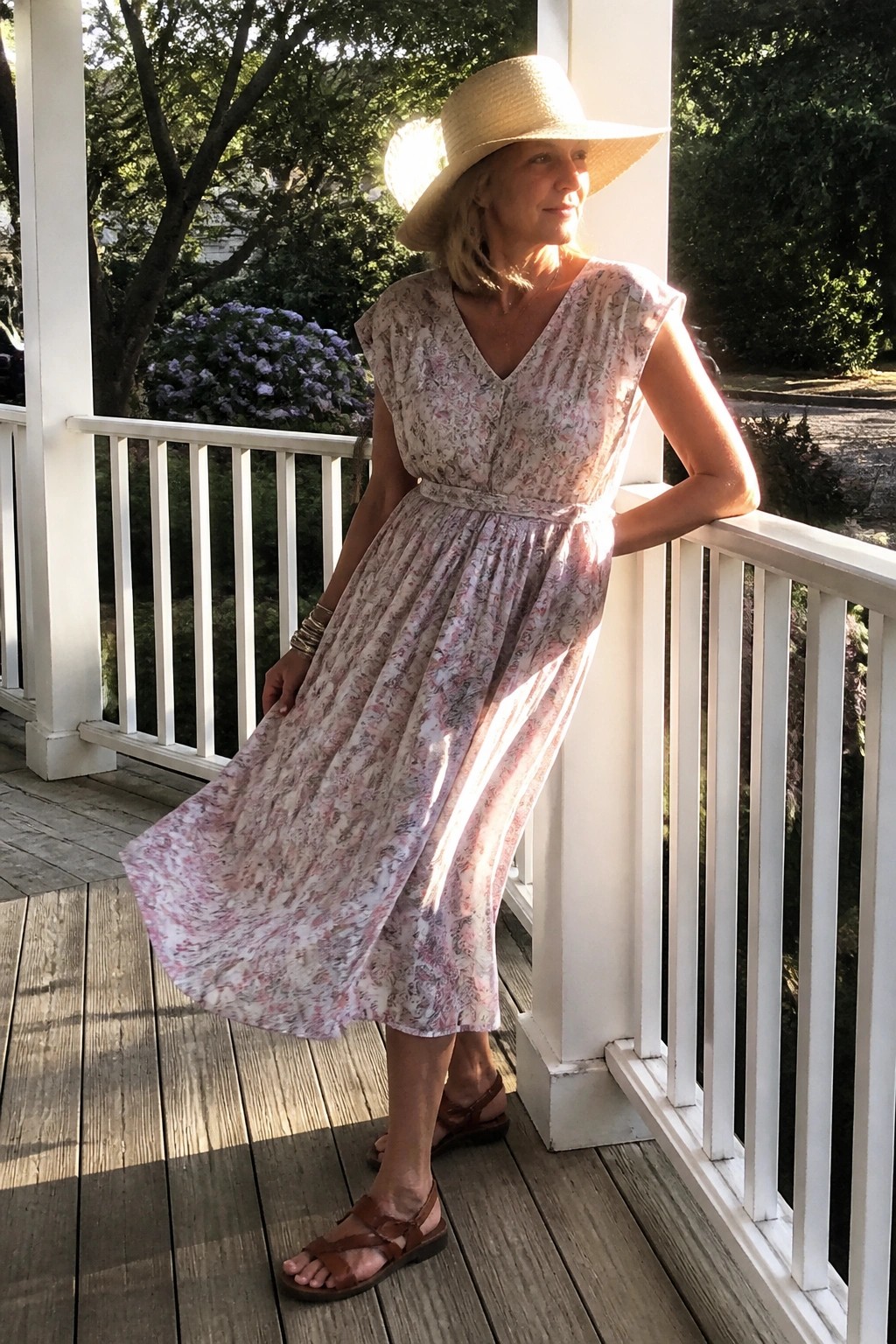 Woman in pink floral dress and straw hat on sunny white porch