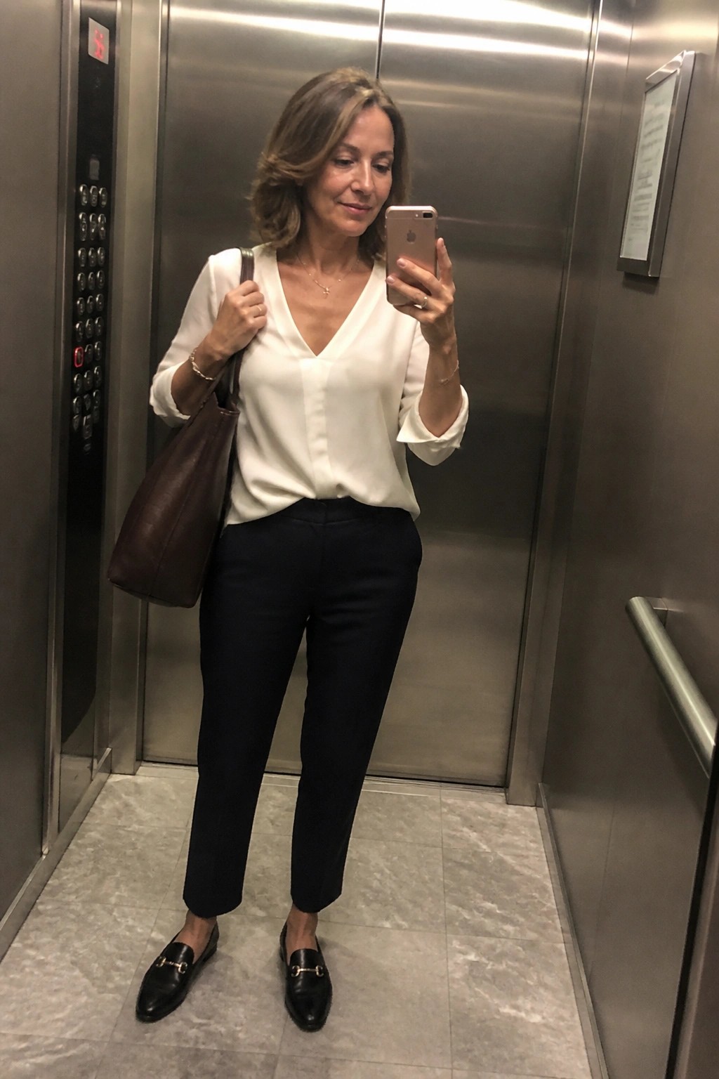 Woman in white blouse taking selfie in elevator with brown leather bag