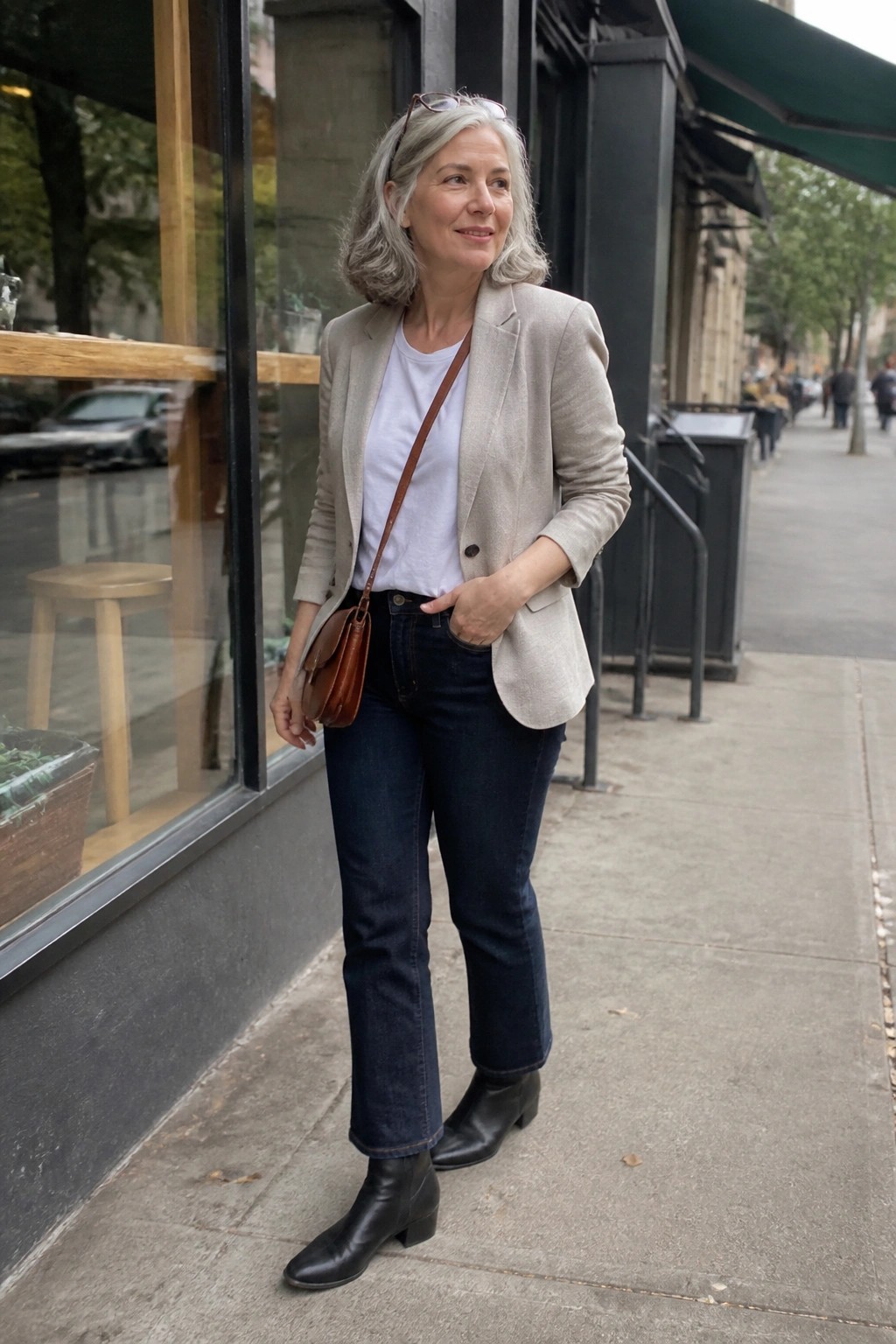 Gray-haired woman in beige blazer and dark jeans outside glass storefront