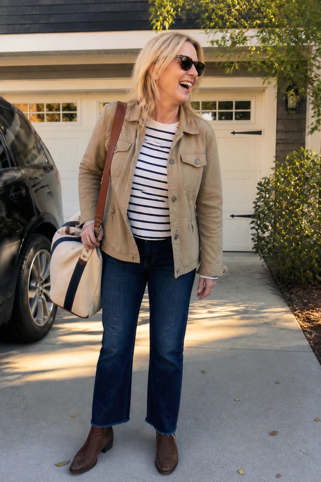 Blonde woman in tan jacket and striped shirt carrying bag on driveway
