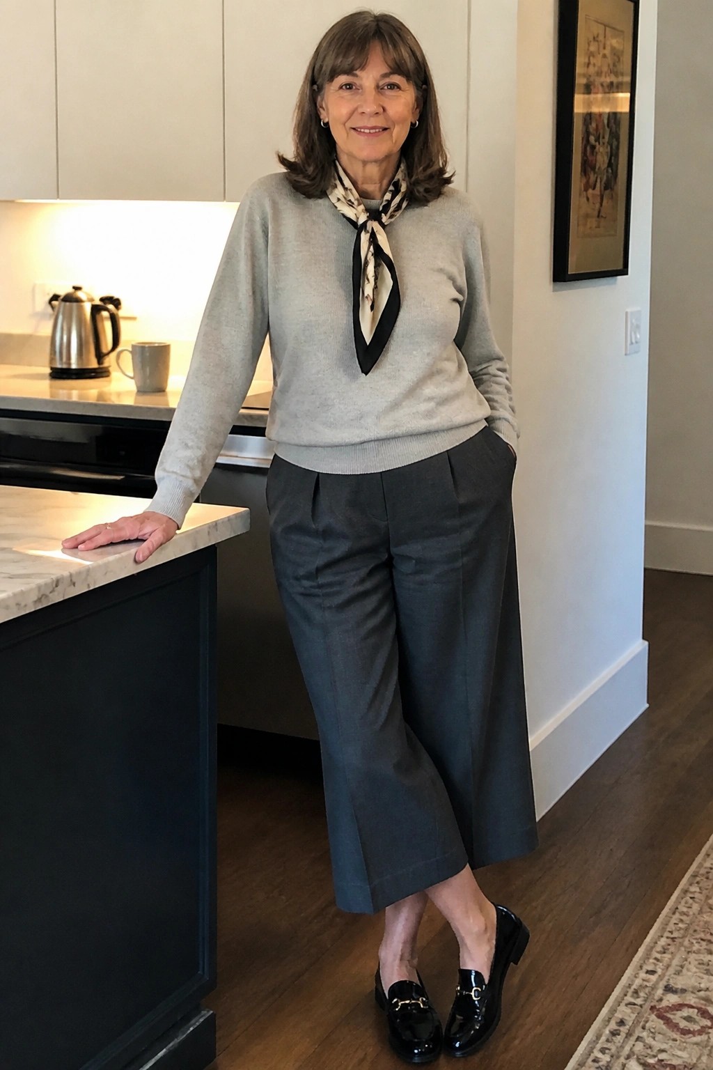 Woman in gray sweater with scarf and wide-leg pants standing in kitchen