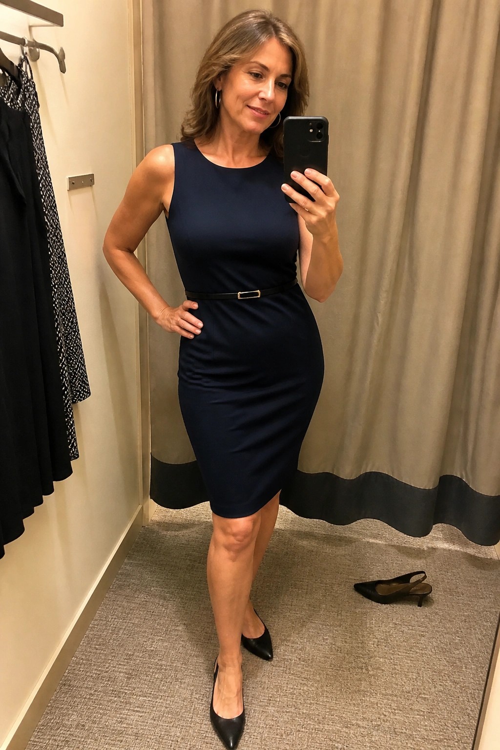 Woman in navy dress taking mirror selfie in fitting room with black heels