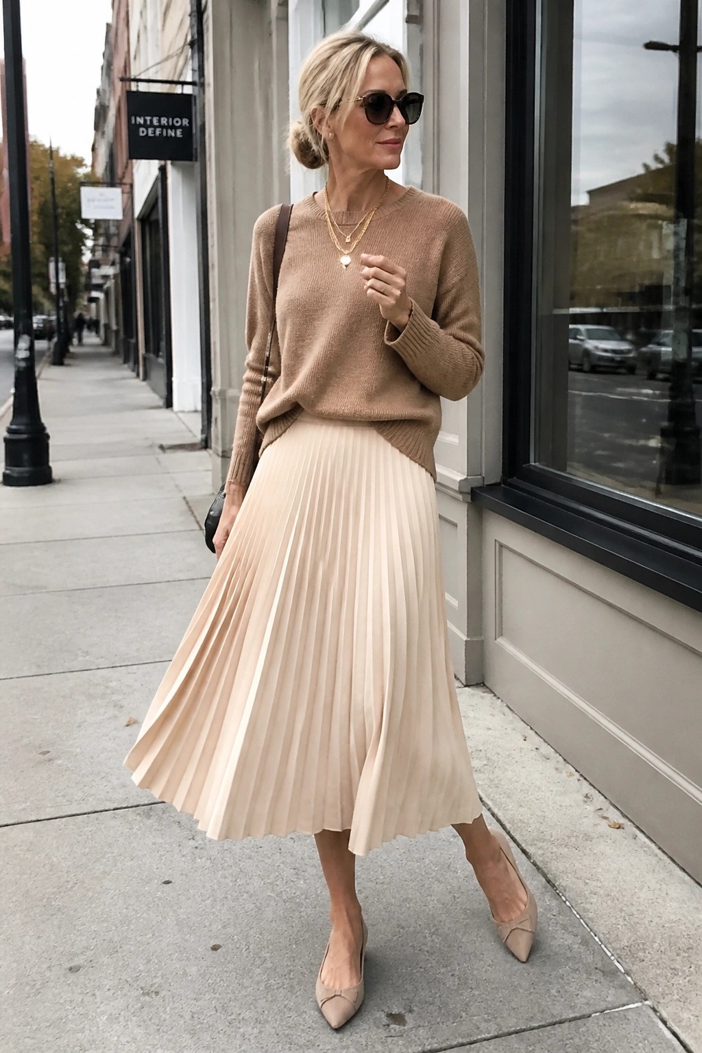 Blonde woman in beige sweater and pleated skirt on city sidewalk