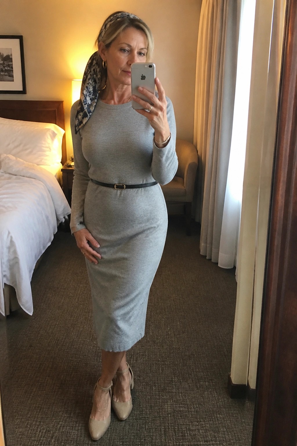 Woman in gray midi dress with headscarf taking mirror selfie in hotel room