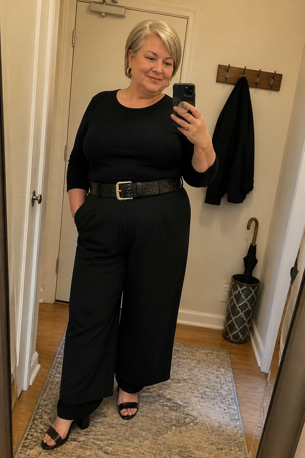 Woman with short gray hair in black outfit and studded belt taking mirror selfie