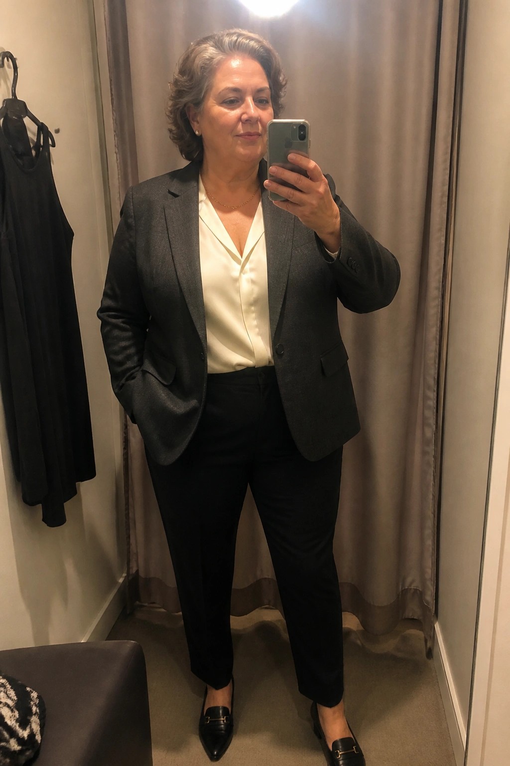 Woman with gray hair in gray blazer and black pants taking a mirror selfie.