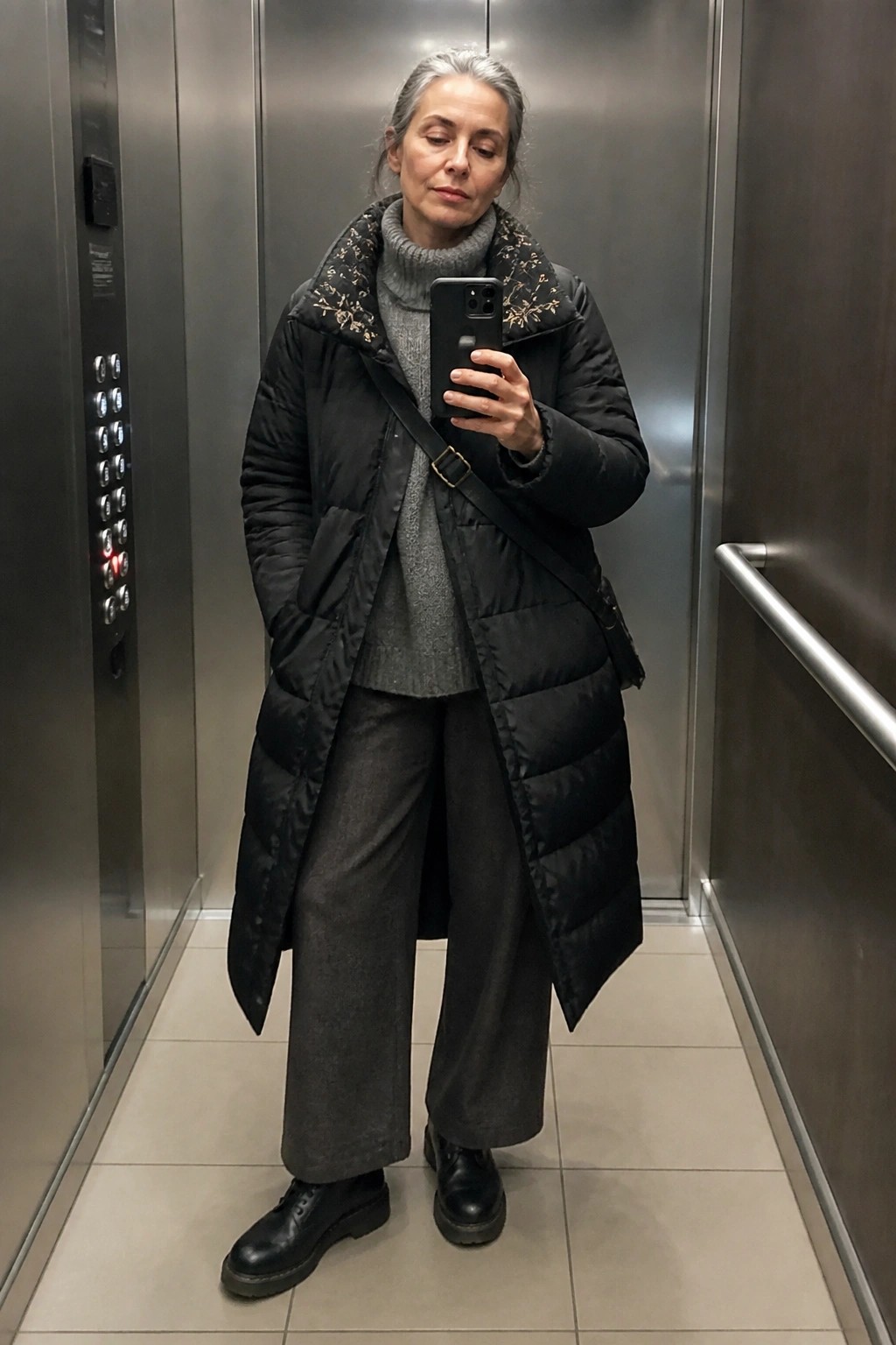 Gray-haired woman in black puffer coat taking selfie in elevator