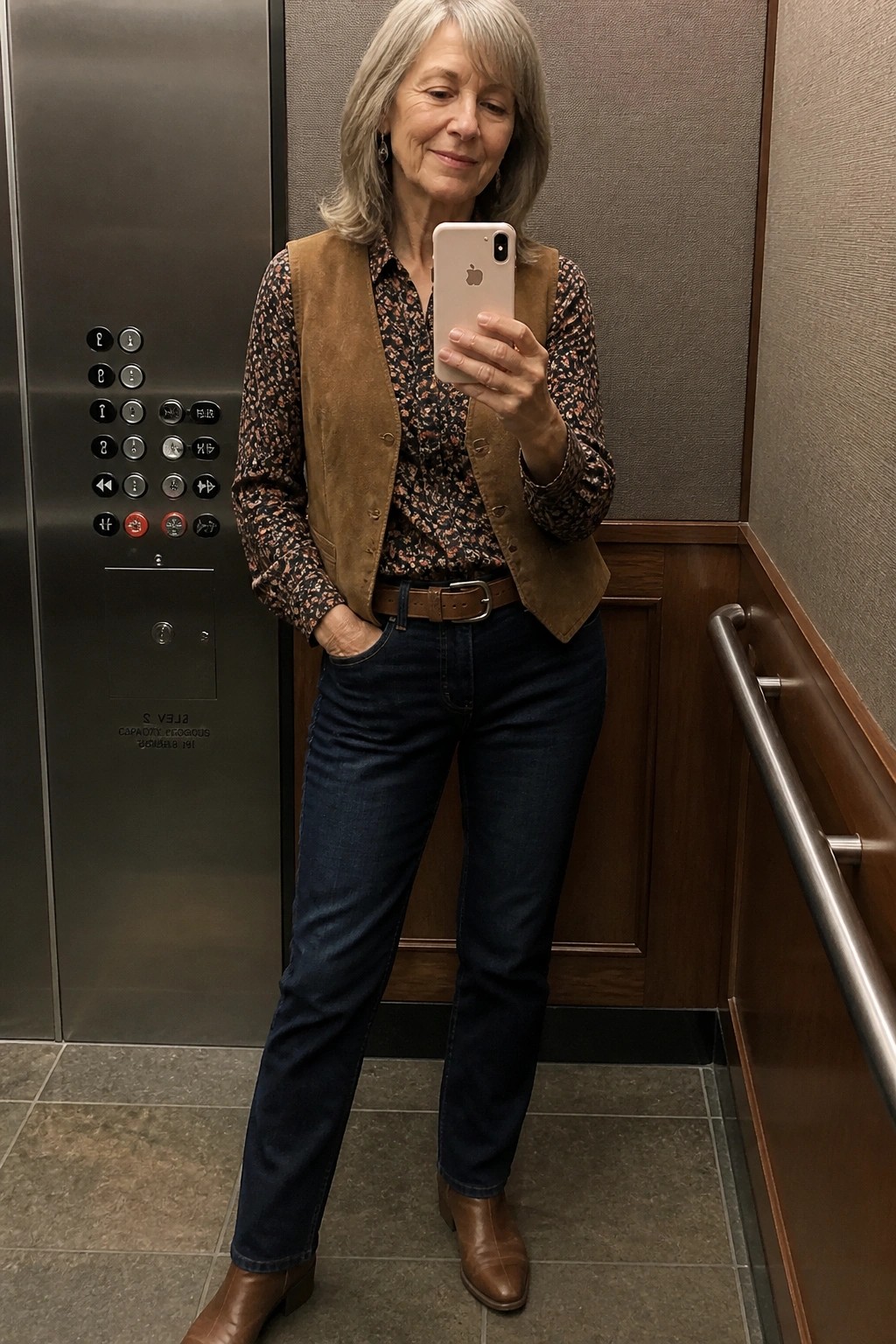 Woman with gray hair in brown vest and blue jeans taking selfie in elevator