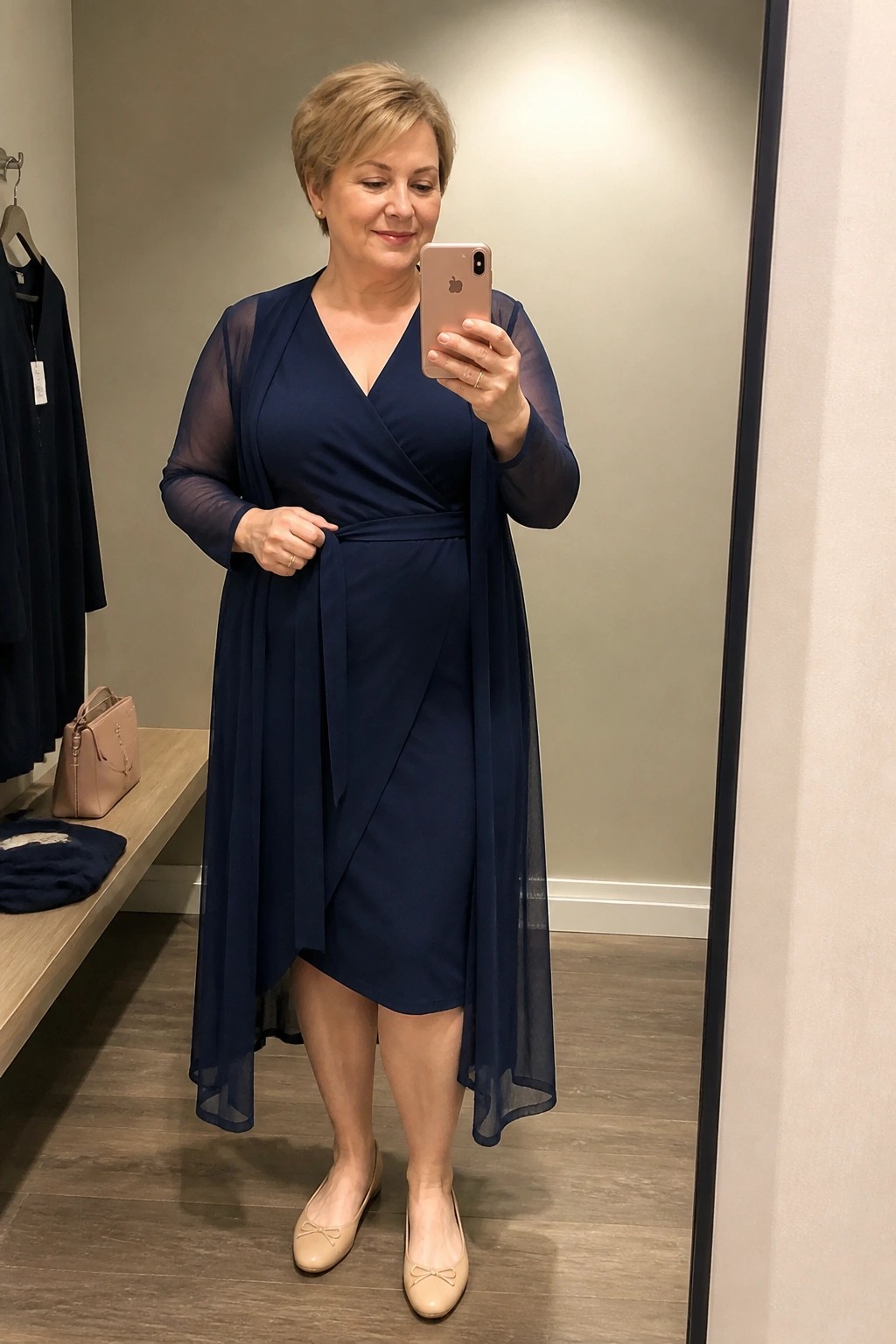 Woman in navy wrap dress with sheer sleeves taking mirror selfie in fitting room
