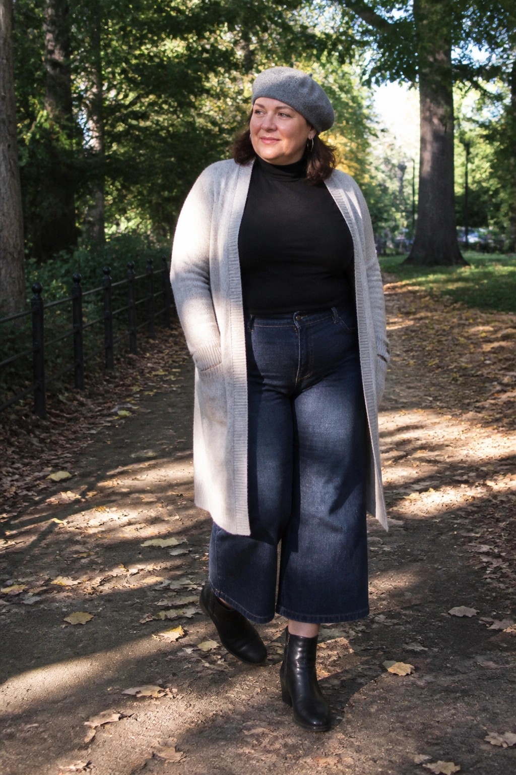 Woman in gray beret and cardigan with wide-leg jeans on autumn park path