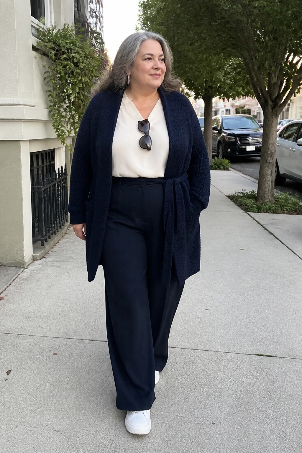 Gray-haired woman in navy belted cardigan and wide pants on sidewalk.
