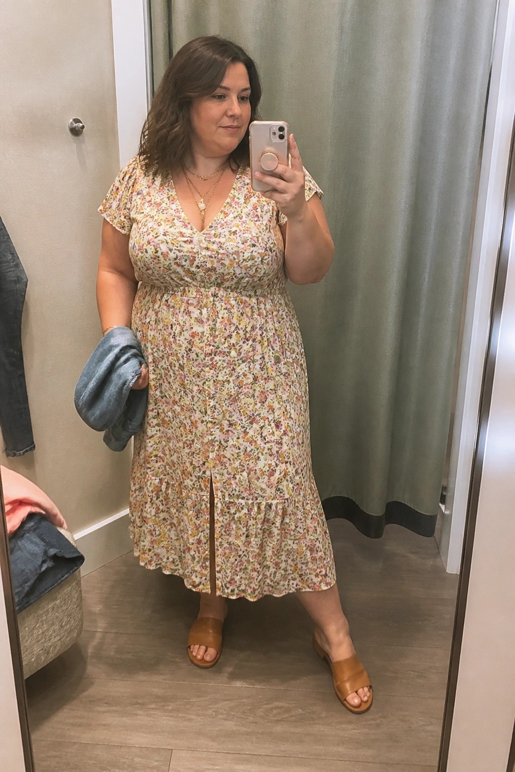 Woman in floral midi dress taking mirror selfie in fitting room wearing sandals