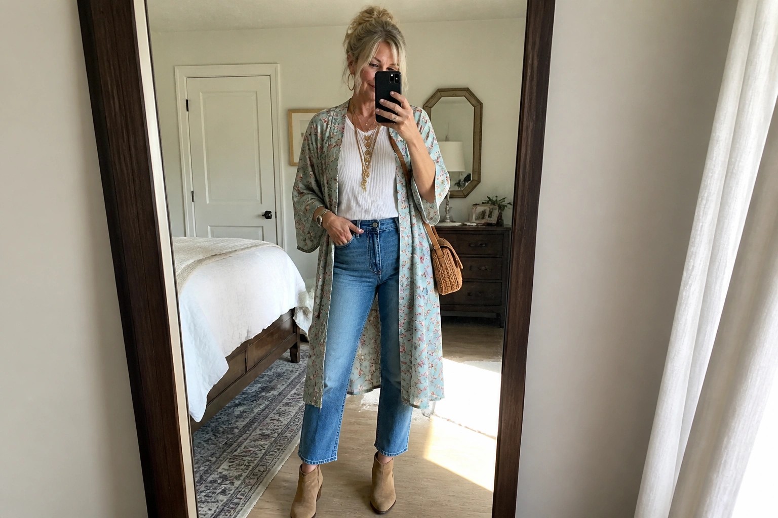 Blonde woman in floral kimono cardigan, white top, and jeans taking mirror selfie.