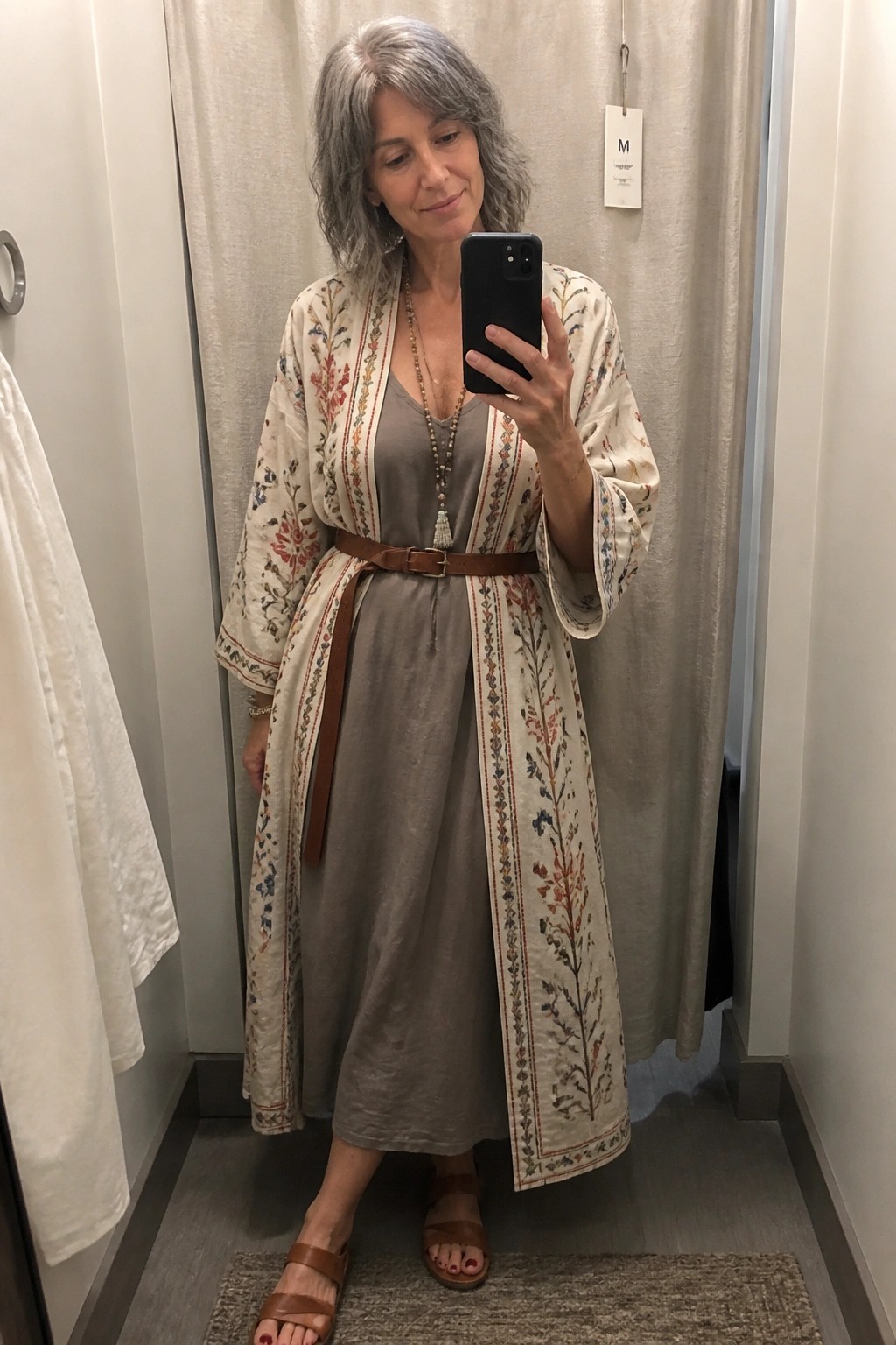 Gray-haired woman in floral kimono over gray dress taking mirror selfie with phone