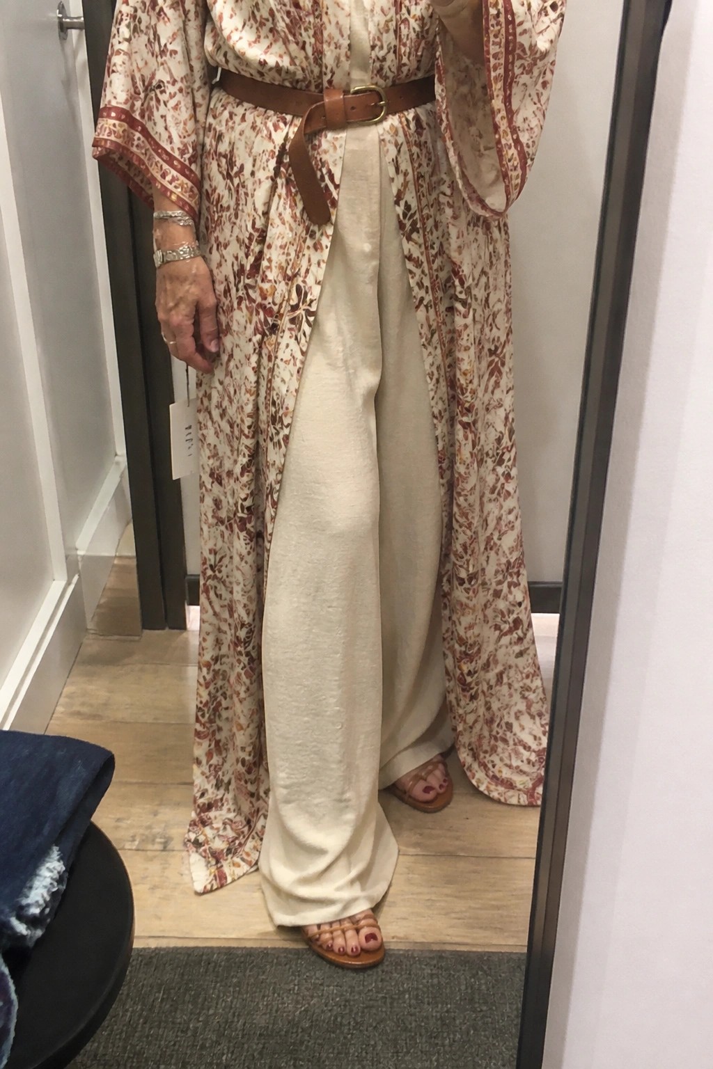 Woman in floral kimono robe over cream wide-leg pants with brown belt and sandals.