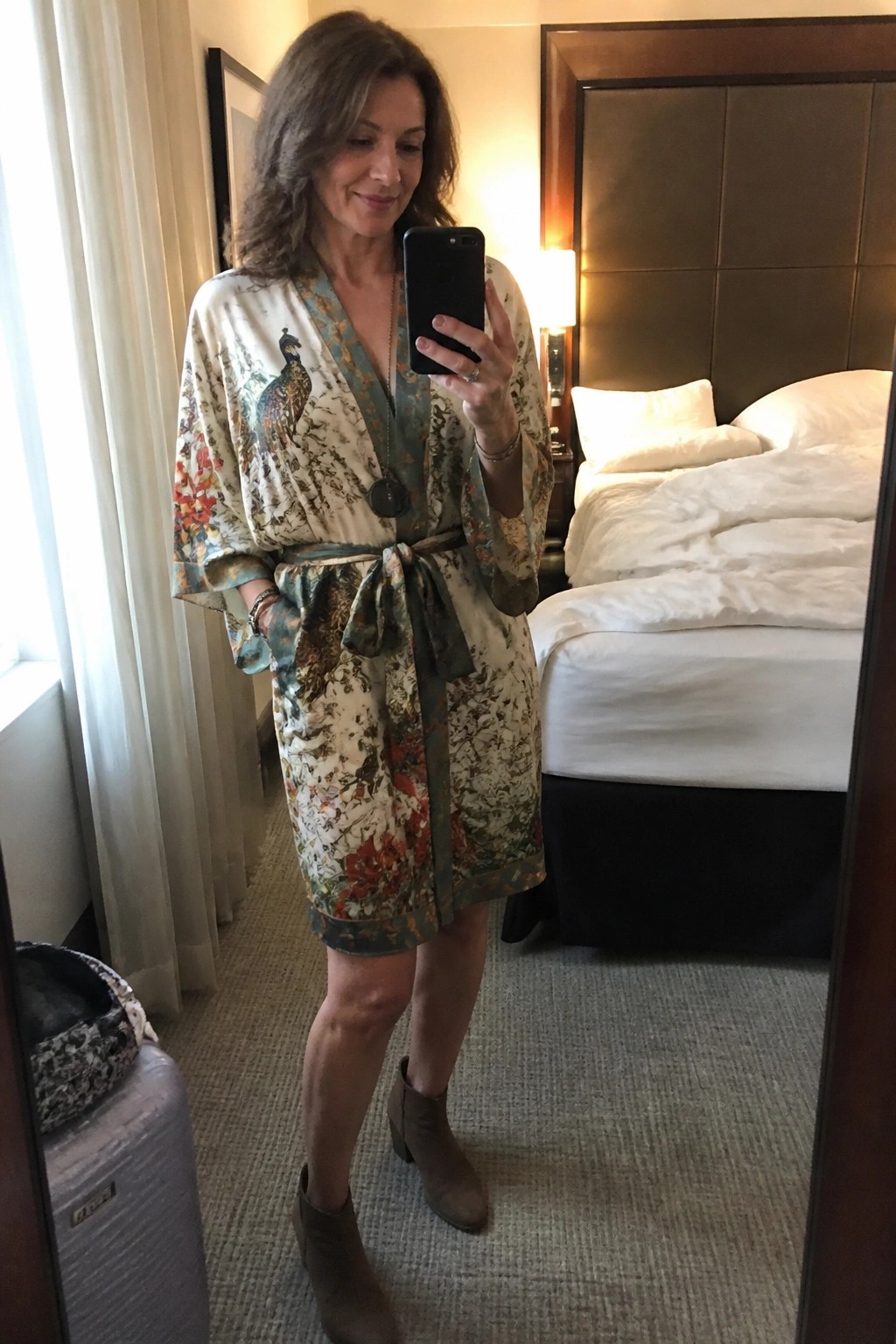 Woman in floral peacock robe taking mirror selfie in hotel room.