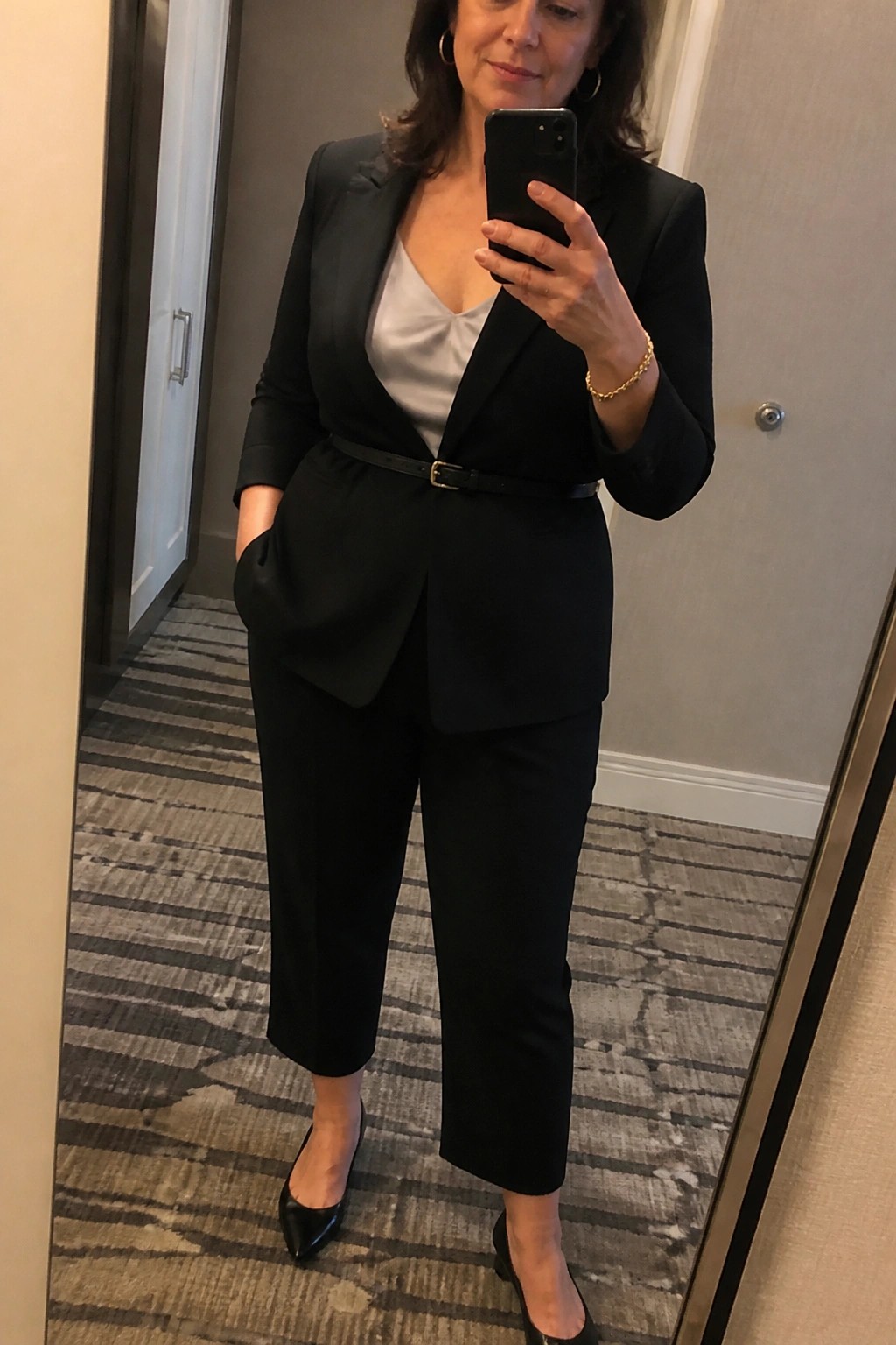Woman in black pantsuit with white camisole taking mirror selfie with phone