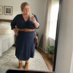 Woman in navy wrap dress with brown belt taking bedroom mirror selfie