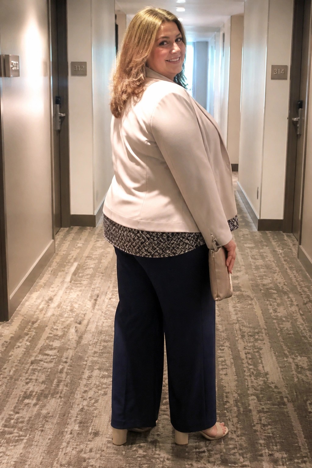 Woman in beige blazer and navy pants standing in hotel hallway