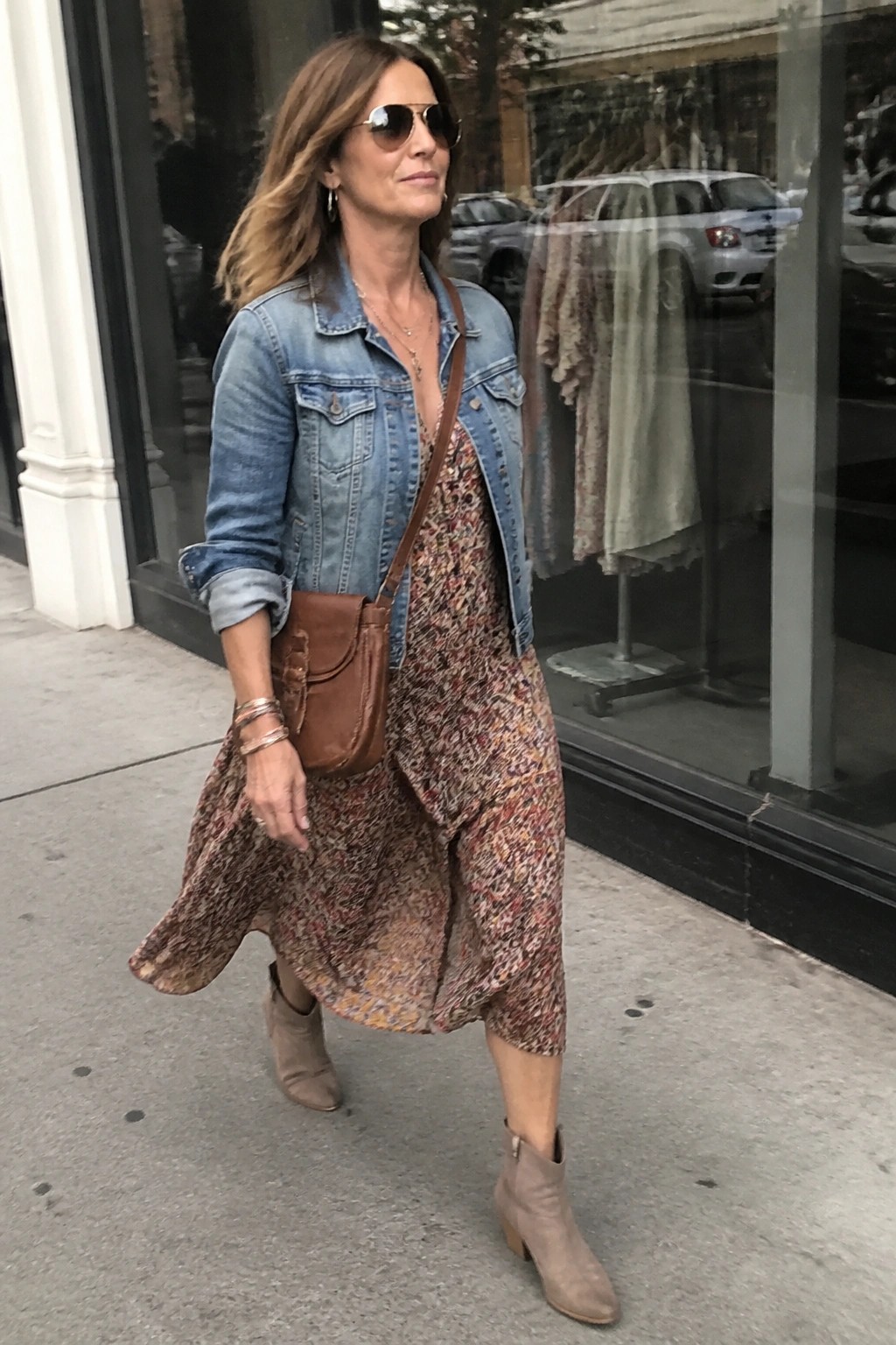 Woman in floral dress and denim jacket walking on city sidewalk