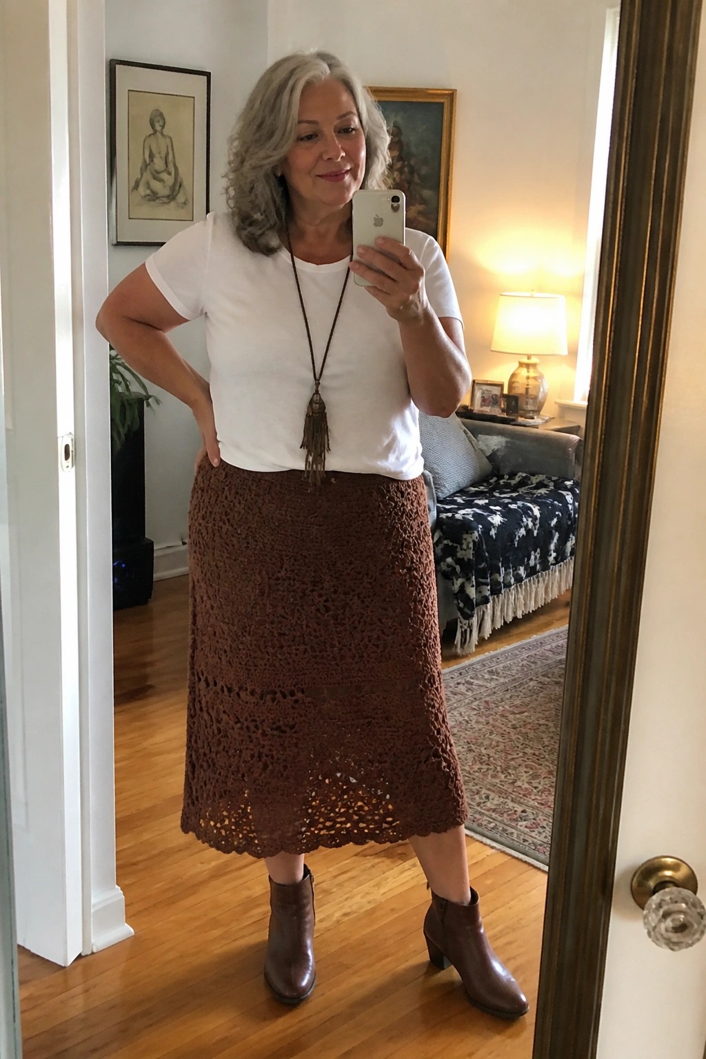 Woman with gray hair in white top and brown crochet skirt taking mirror selfie