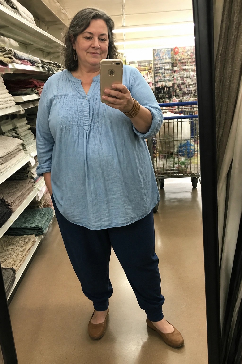 Woman with gray hair in light blue blouse taking mirror selfie in store aisle
