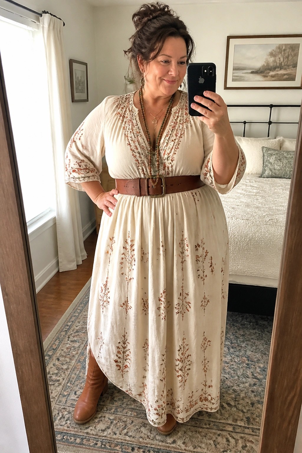 Woman in cream floral maxi dress with brown belt and boots taking bedroom mirror selfie