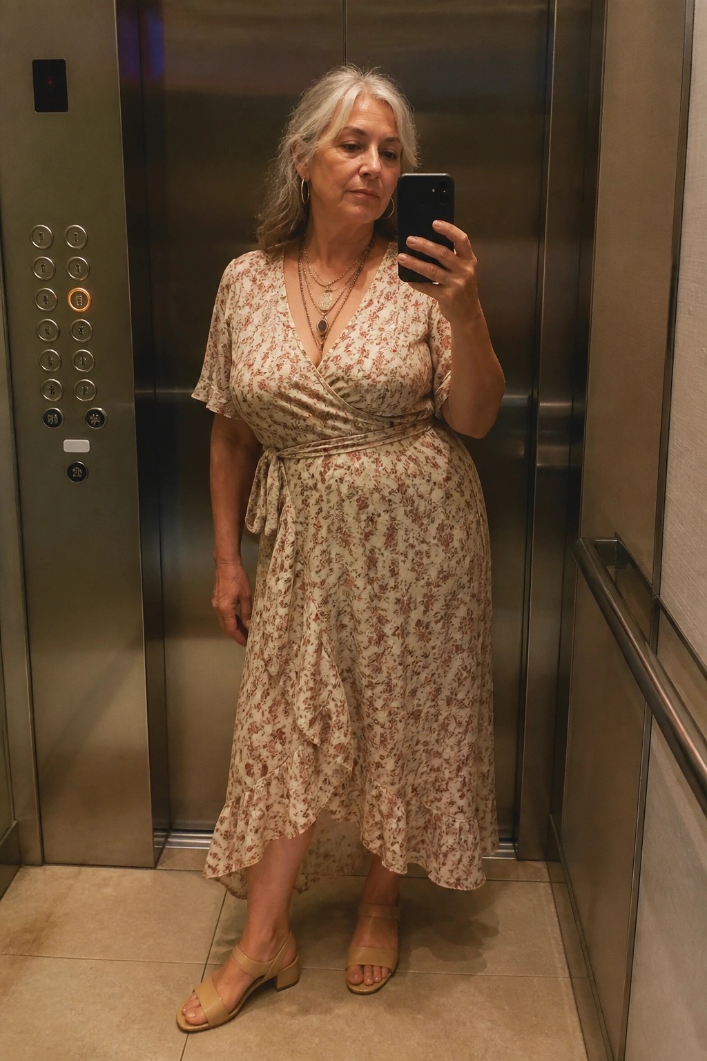 Gray-haired woman in floral wrap dress taking selfie inside elevator