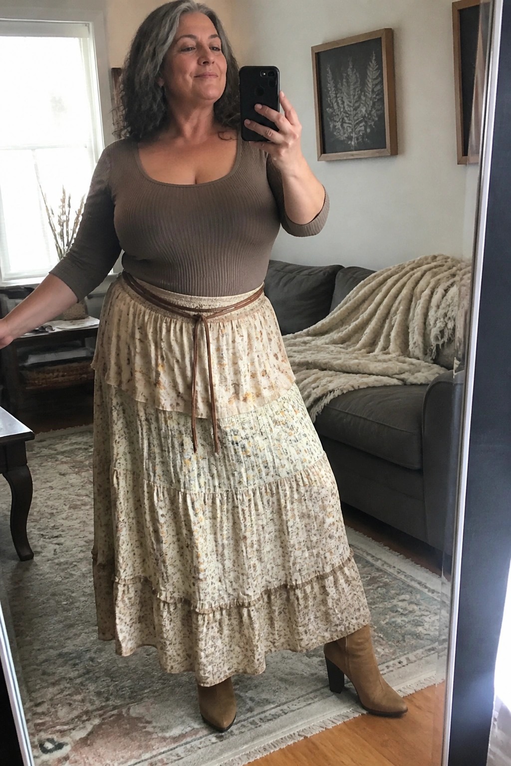 Woman with gray hair in brown top and floral tiered skirt taking mirror selfie