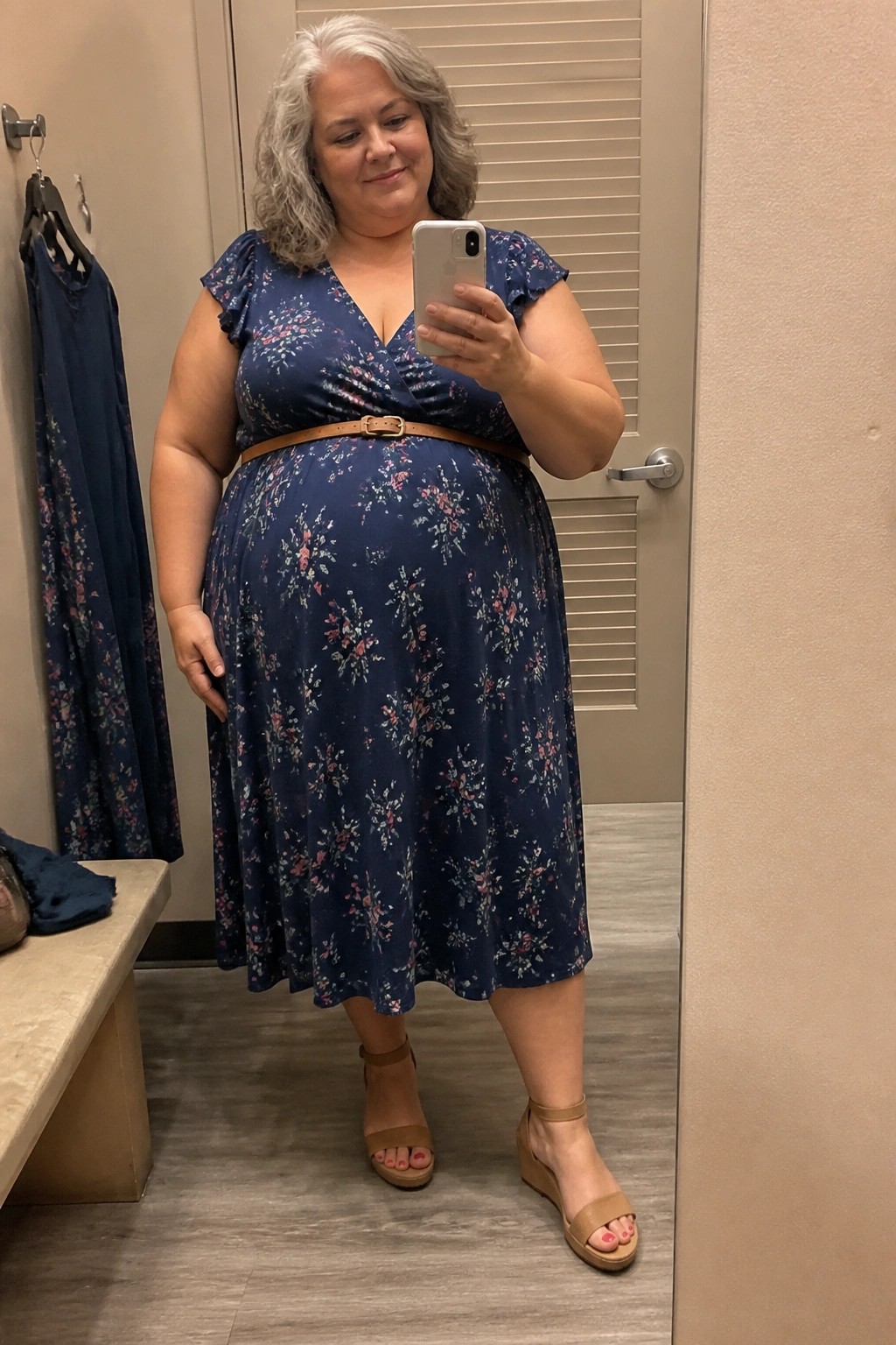Woman with gray hair in blue floral dress taking mirror selfie in fitting room