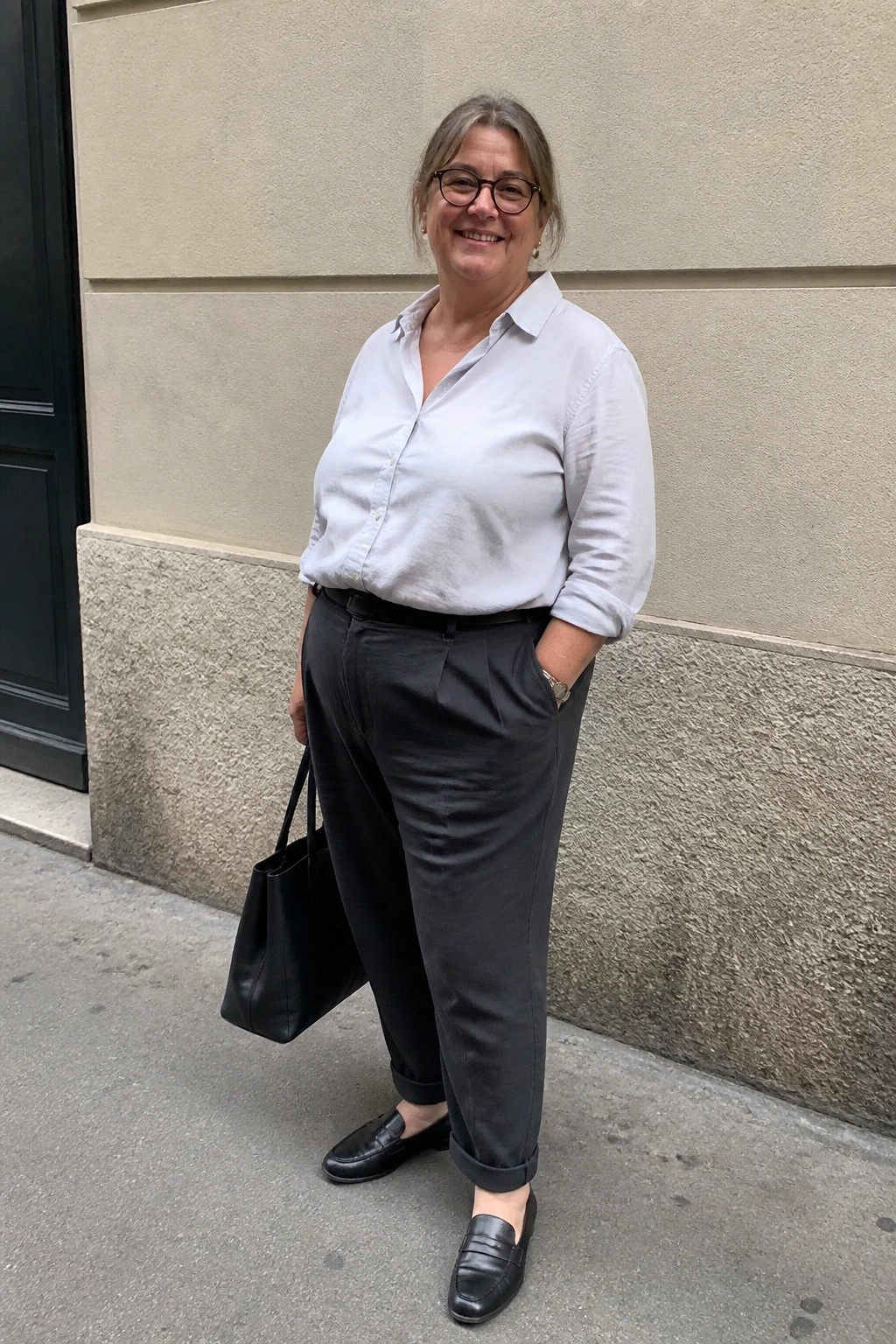 Smiling woman in light blue shirt and dark pants holding black tote bag outdoors