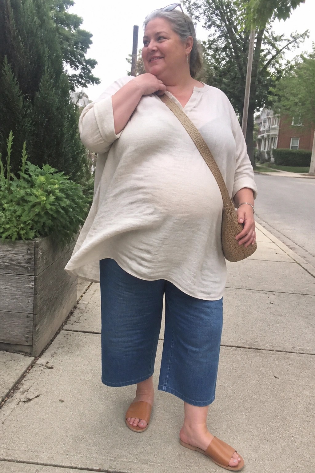Gray-haired woman in loose white top and blue capri pants on sidewalk