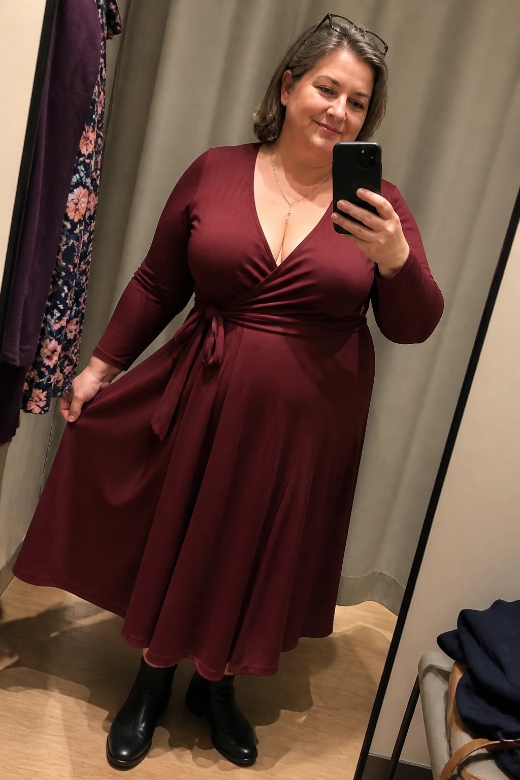 Woman in burgundy wrap dress taking mirror selfie wearing black boots