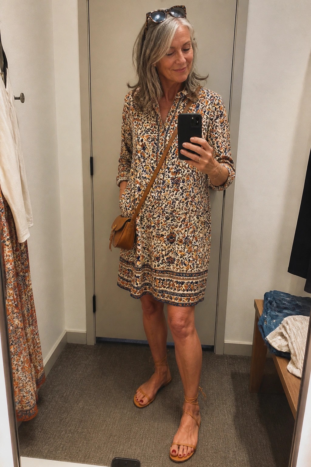 Gray-haired woman in floral print dress taking mirror selfie in dressing room
