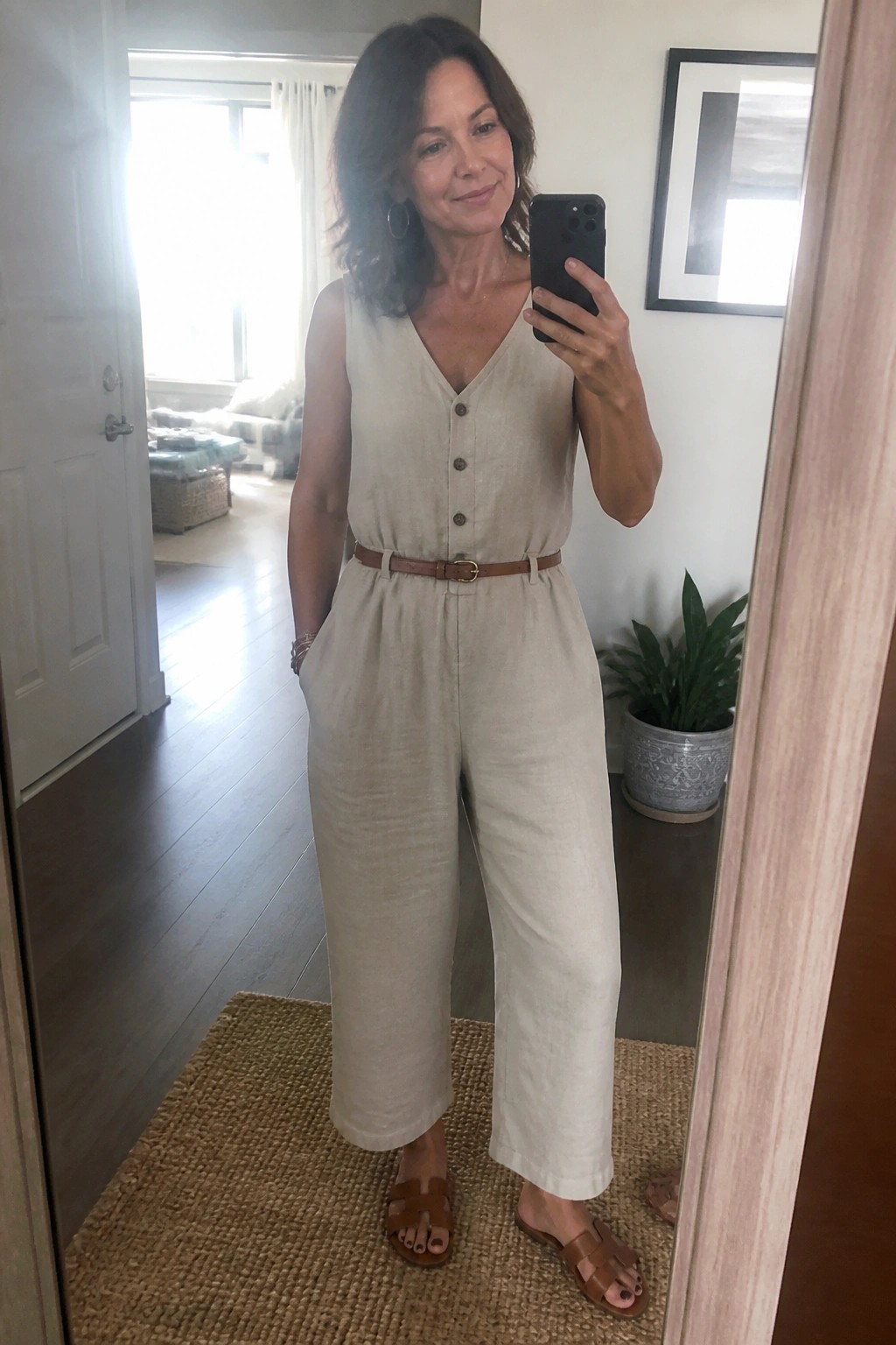 Woman in beige belted jumpsuit takes mirror selfie wearing brown sandals