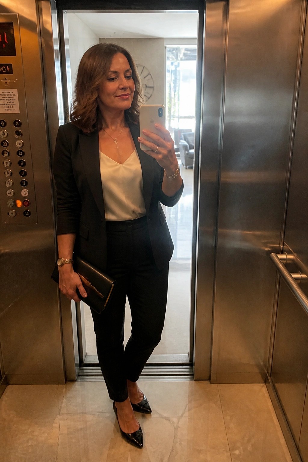 Woman in black blazer taking selfie inside metallic elevator with clutch