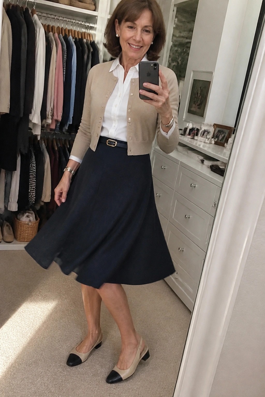 Smiling woman in beige cardigan and navy skirt holding phone in closet