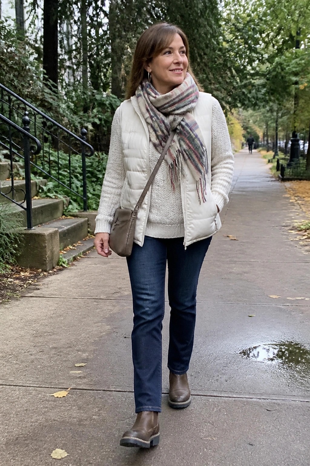 Woman in white puffer vest, plaid scarf, jeans, and boots on wet park path.