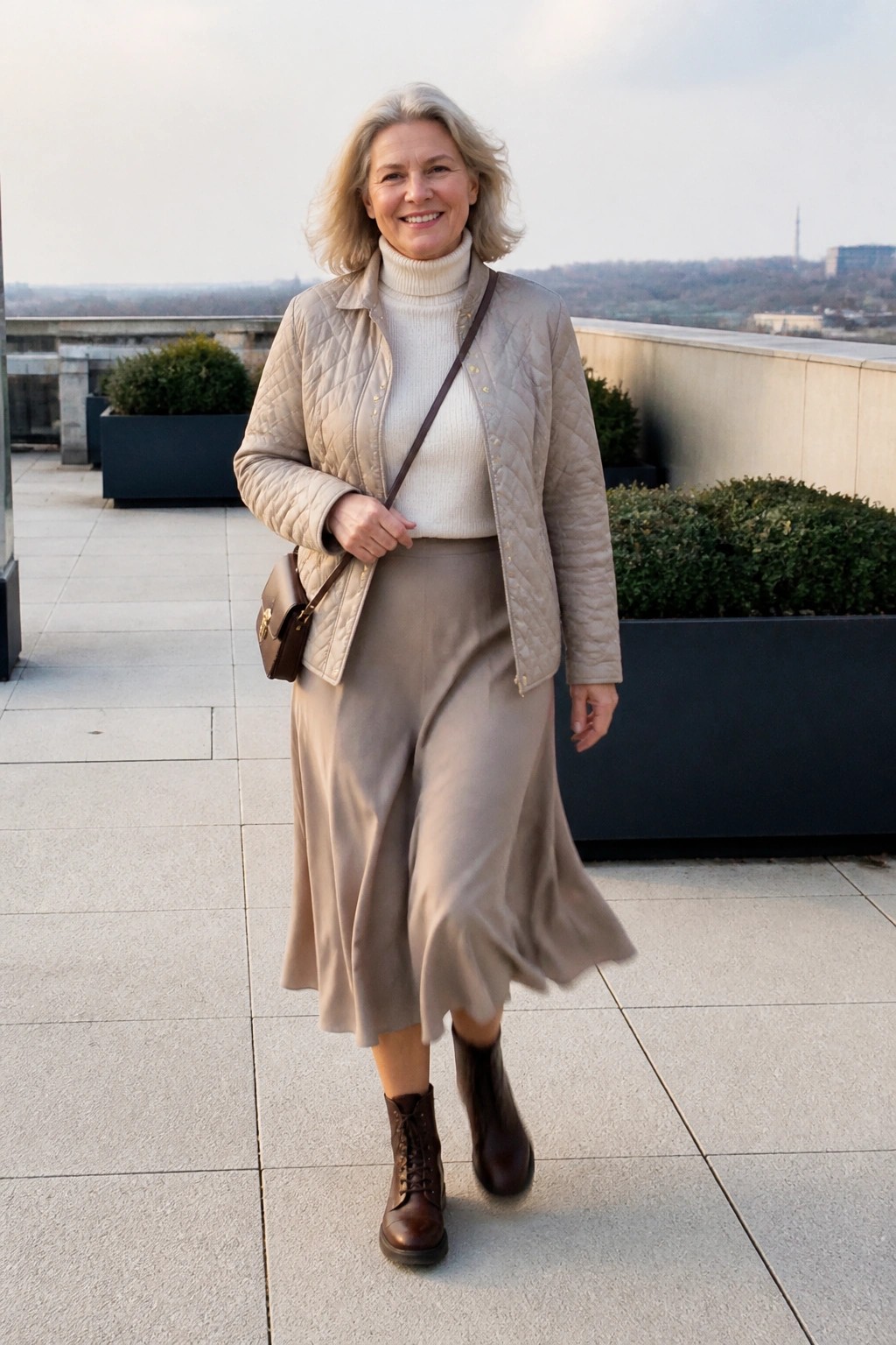 Smiling gray-haired woman in beige quilted jacket, turtleneck, and midi skirt on rooftop terrace